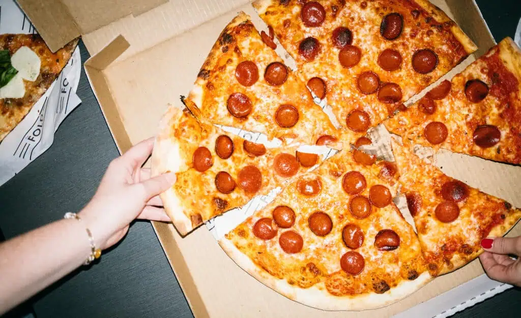 a box of pepperoni pizza photographed from above as multiple people grab slices 