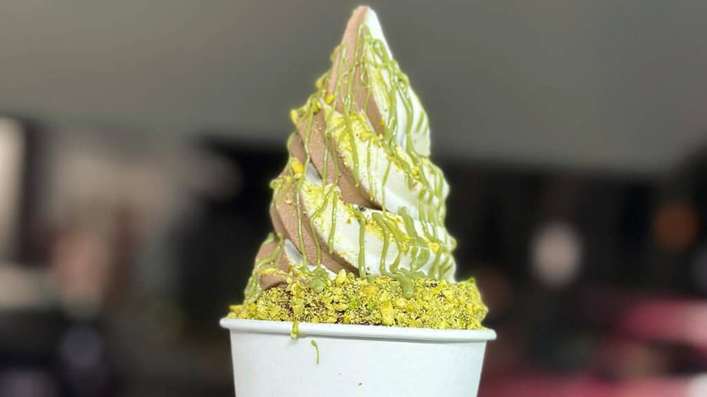 a chimney cake covered in pistachios and filled with vanilla-chocolate soft serve