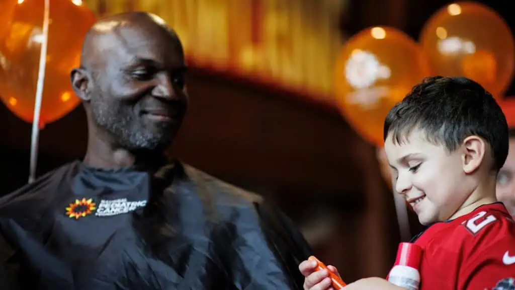 a man sits in a chair at a charity event and prepares to get his hair cut