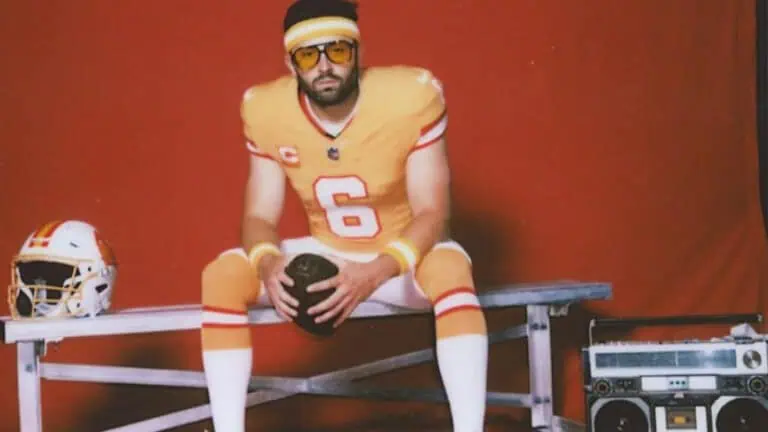 a football player in a light orange jersey poses in a studio.