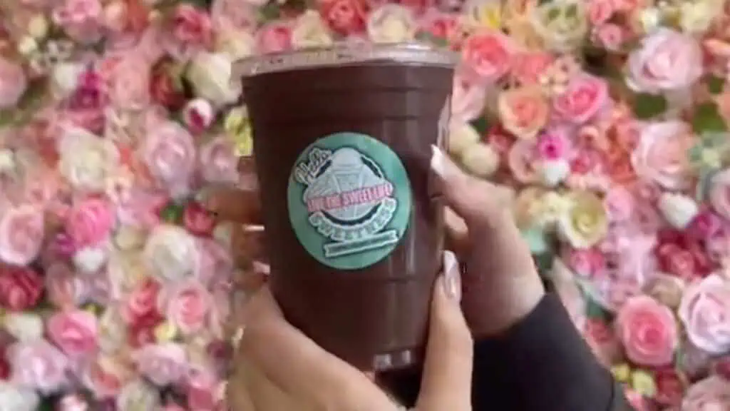 a chocolate coffee drink in front of a flower wall 