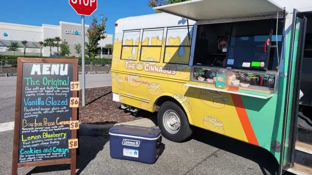 Exterior of a bus converted into a cinnamon roll bakery. It's posted up in a parking lot.