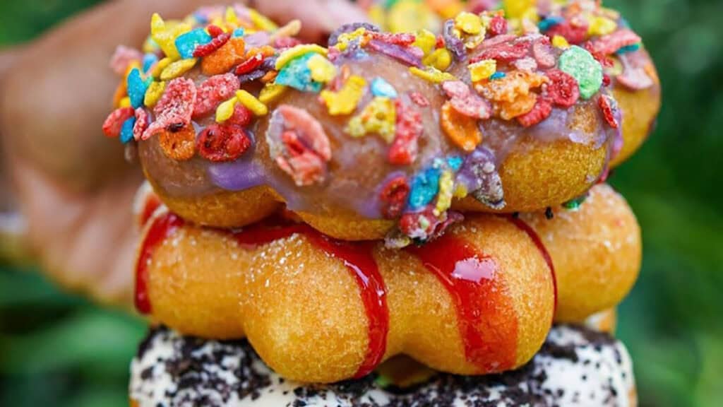 a stack of rice flour donuts covered I chocolate frosting and Fruity Pebbles