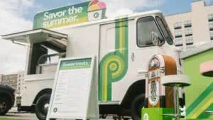 an ice cream truck parked on turf. The truck is white with green stripes