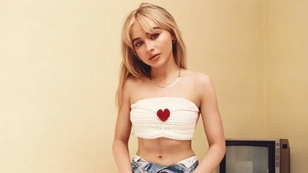 a perfumer with blonde hair in a white tank top poses in front of a plain wall