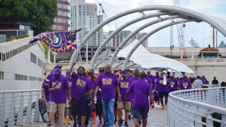 a group of people march in purple shirts on the Riverwalk
