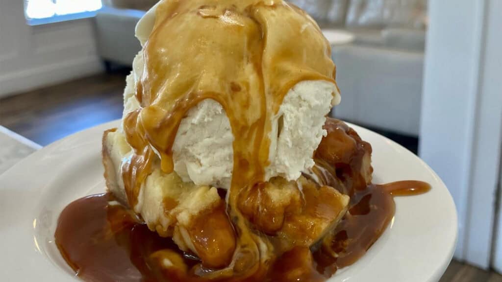 a piece of toffee covered in caramel with a big scoop of vanilla ice cream on top