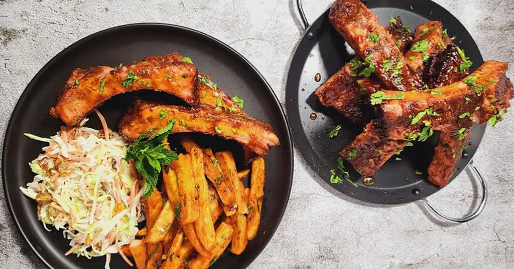 a plate of ribs and veggies on a black plate