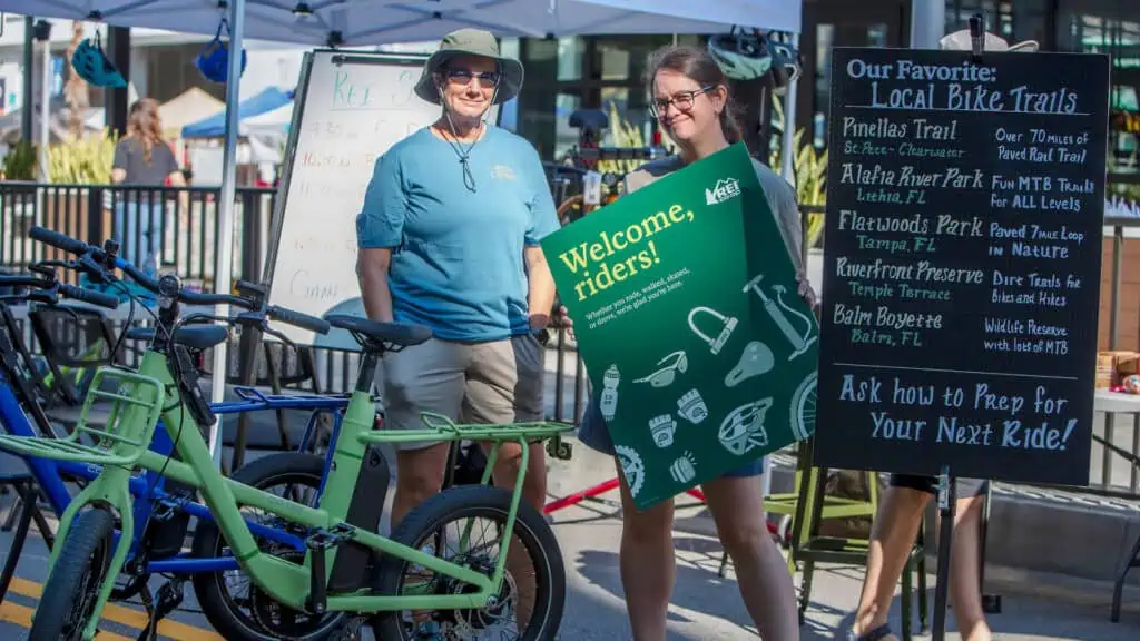 Two people pose in front of a bicycle parking service at an outdoor event