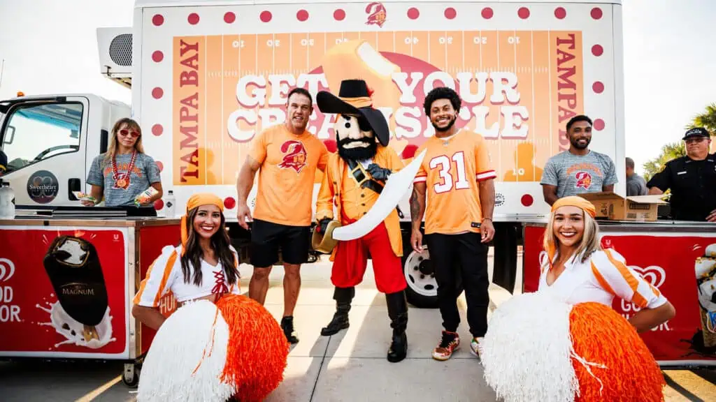 people in bright orange NL jerseys sell merch at a tailgating event