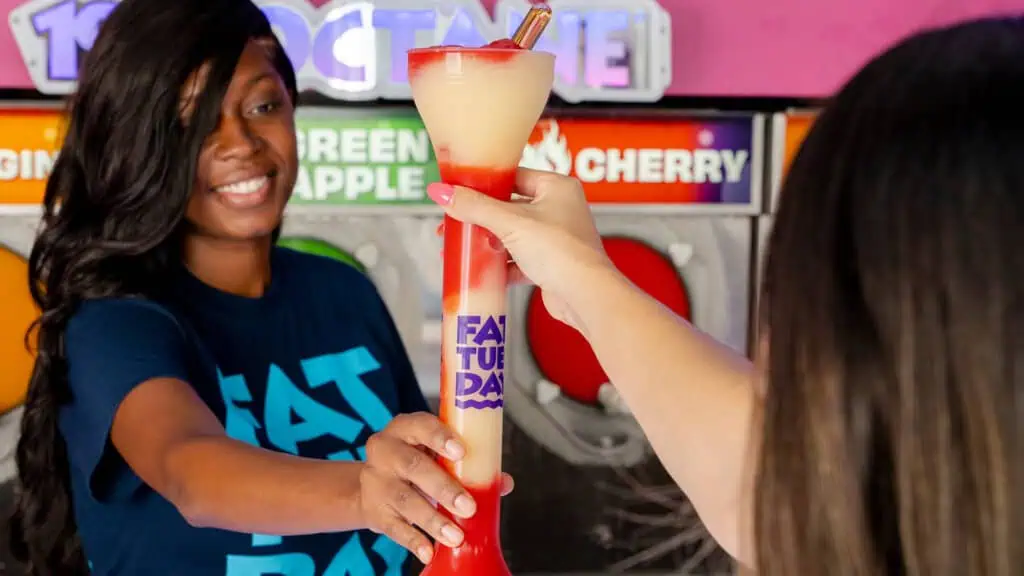 a bartender hands over a large frozen drink in a souvenir cup