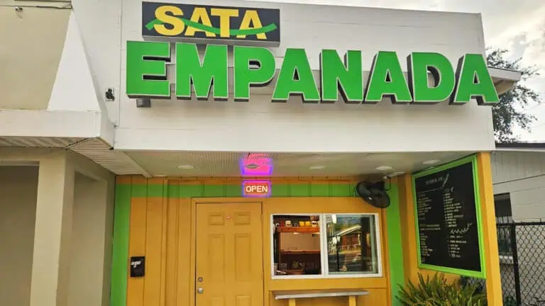 exterior of an empanada order window with a large green sign over the front door