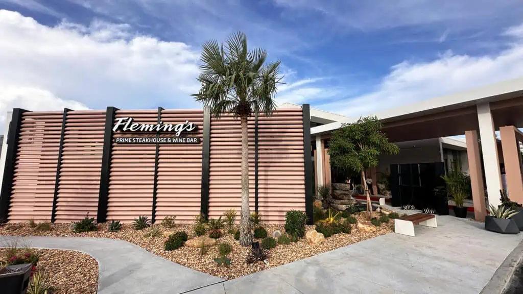 exterior of a restaurant with wood siding. A single palm tree rises over the entrance