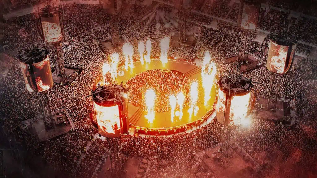 a big concert taking place on a football field, flames surround the stage