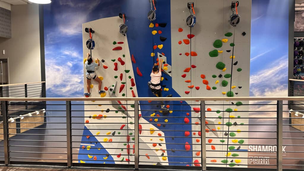 two kids scale a rock wall inside a shopping mall