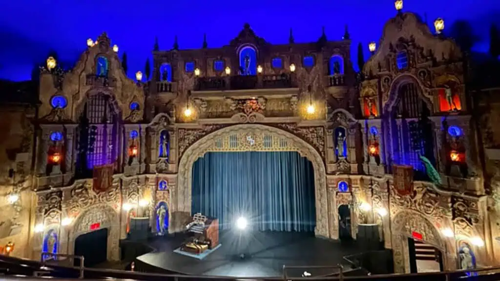 interior of a historic movie theatre with an organ on state and large blue velvet curtains in front of the screen