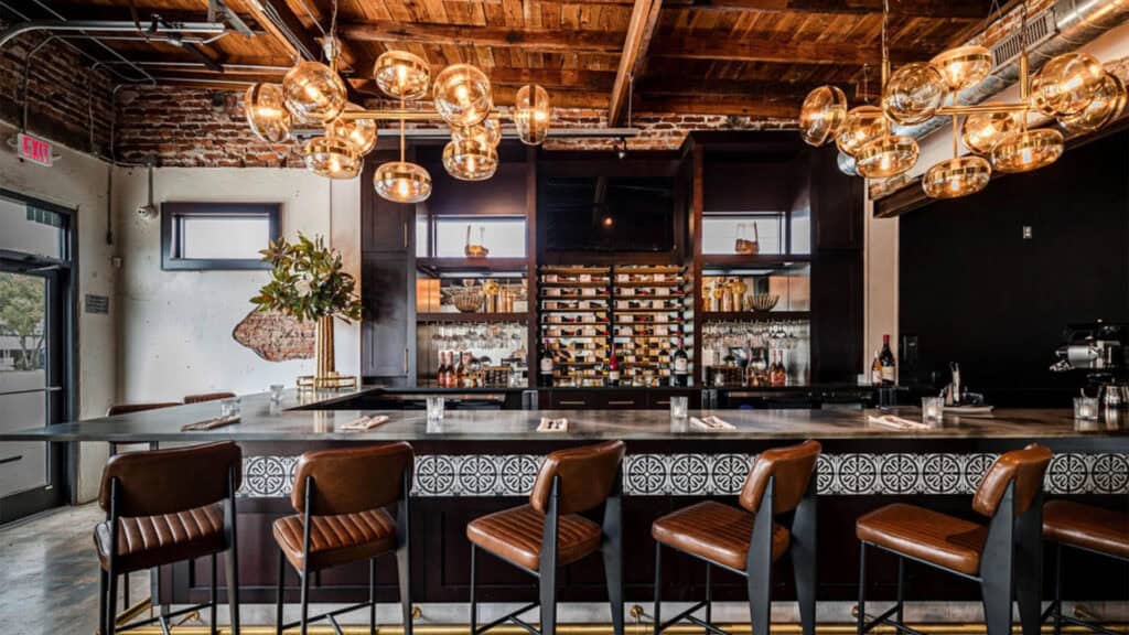 interior of a restaurant with a wrap around wine bar lit with Edison bulbs