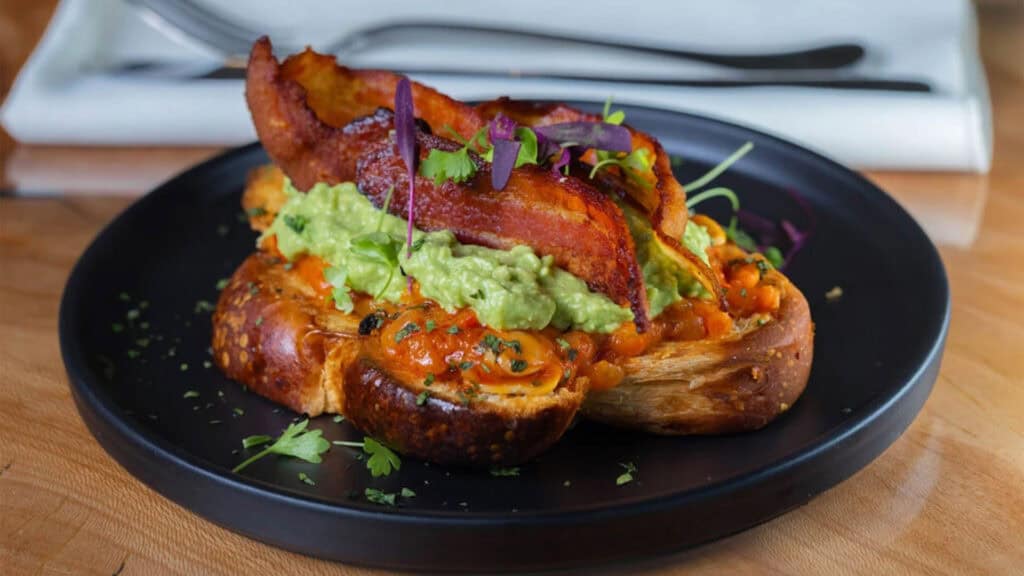 a toast dish with avocado and savory protein on top