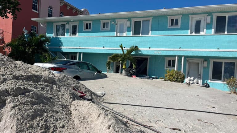 Car under sand in a seaside area after a storm. Blue apartment building is in the back ground