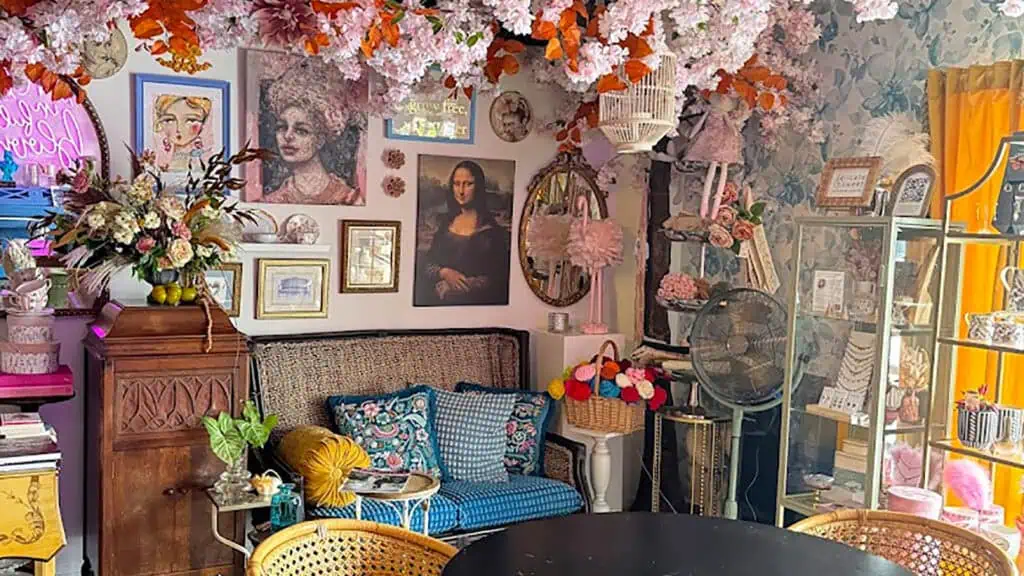 interior of a coffee shop covered in flowers on the wall and framed portraits. A Soft pink light illuminates the pictures.