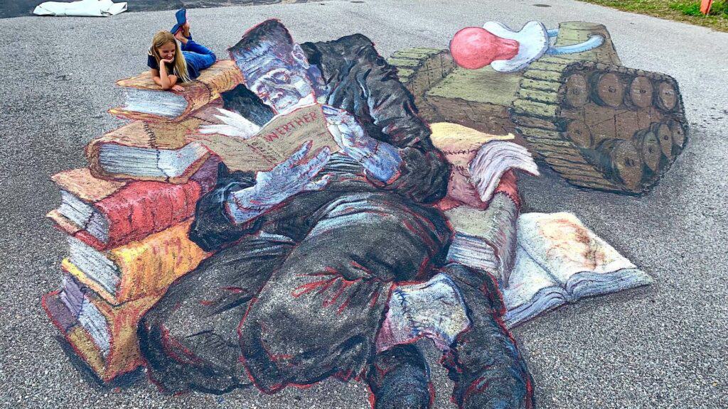 a large 3D mural with a person viewing the mural from the street. The mural shows Frankenstein's monster reading a book 