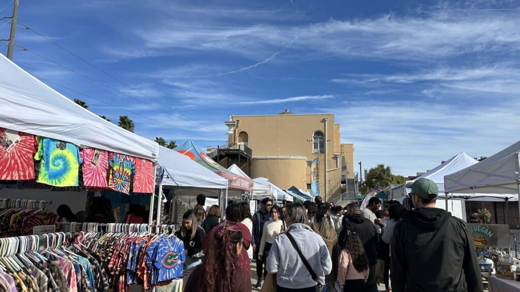 a group of people walk through vendor tents at an open air market