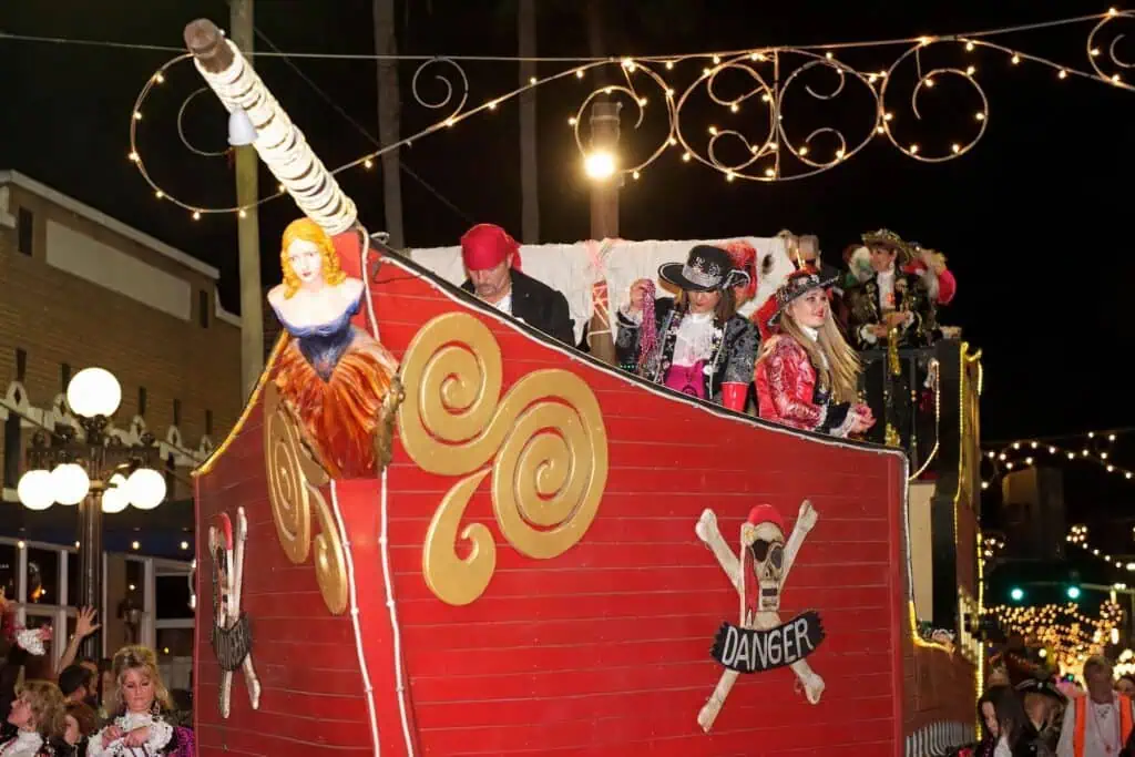 multiple people ride a red pirate ship in a parade