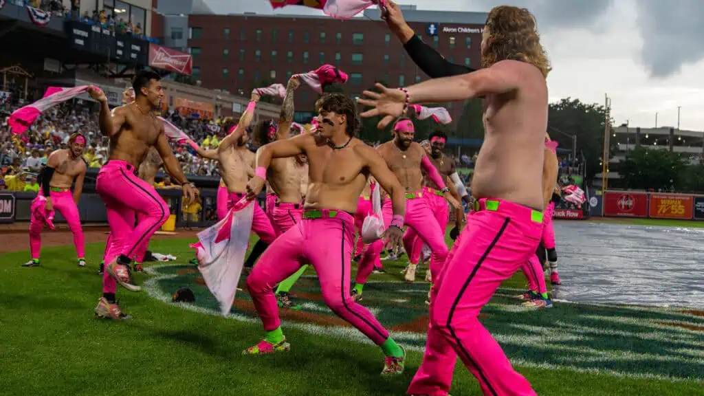 a group of shirtless baseball players dance on the baseball field