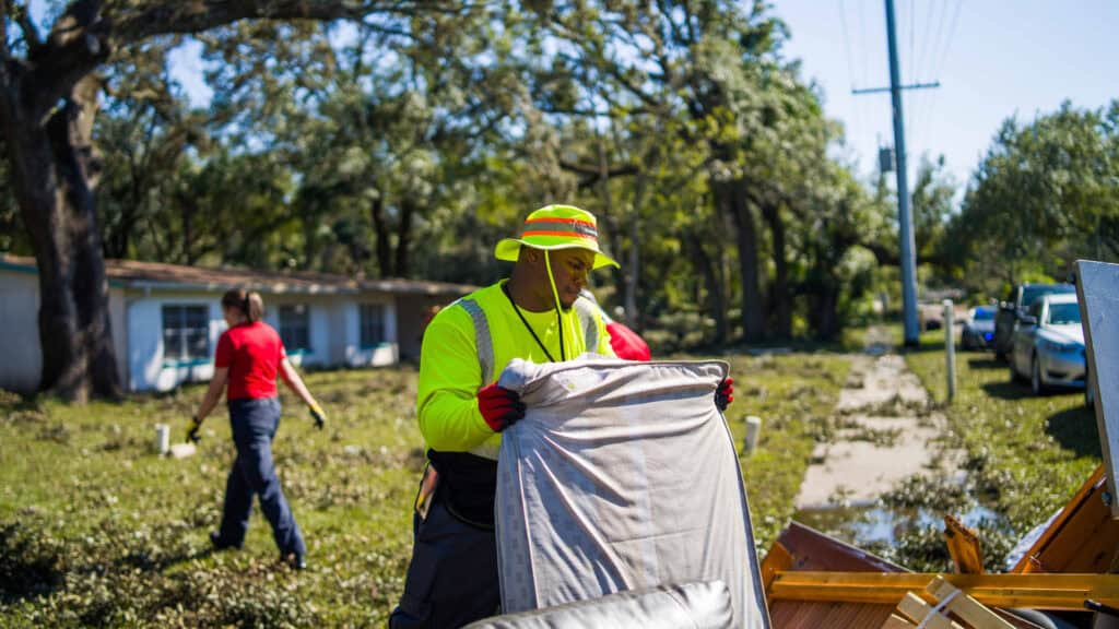 a man in a yellow hat collects debris on the side of the road