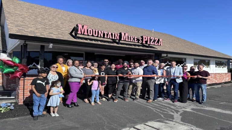 crowd of people cutting ribbon in front of building.