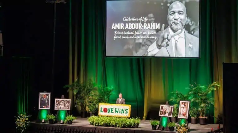 a group of people on stage during a memorial. Green curtains are displayed in the back ground.