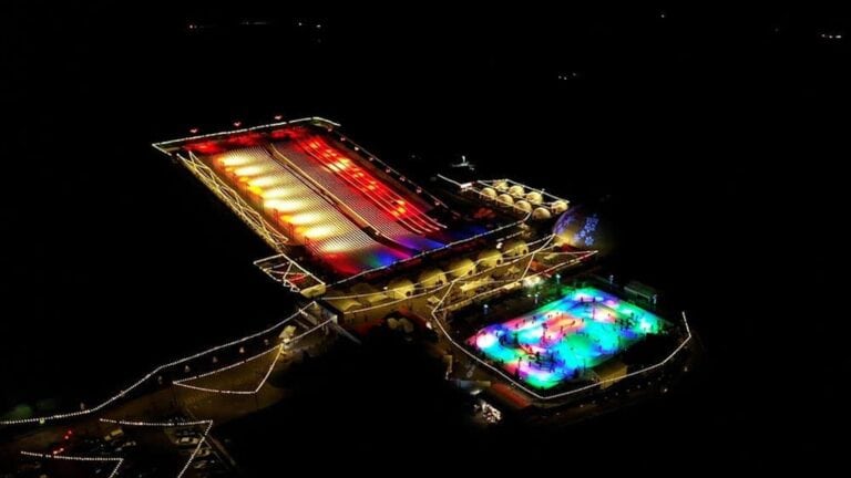 aerial view of a large snow park called Snowcat Ridge illuminated at night. There's a skating rink and a large sledding hill visible