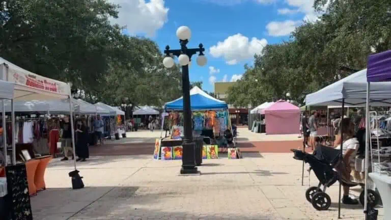 An outdoor market on a sunny day. an old lamp post is at the center of the image