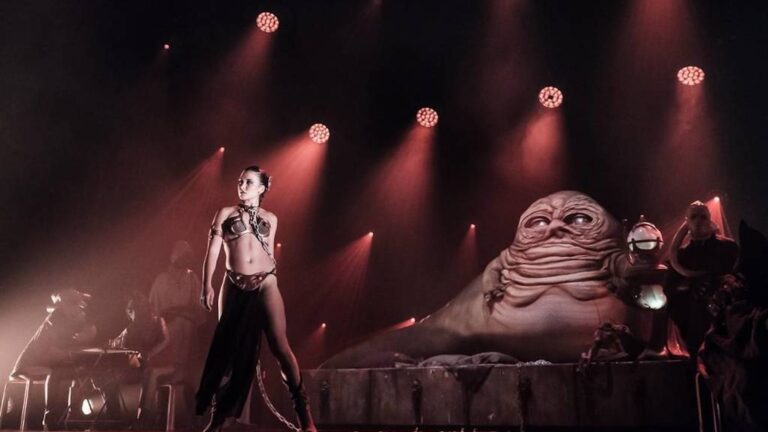 Person on stage under red lights. The stage is set to look like Jabba The Hutt's hideout from Star Wars