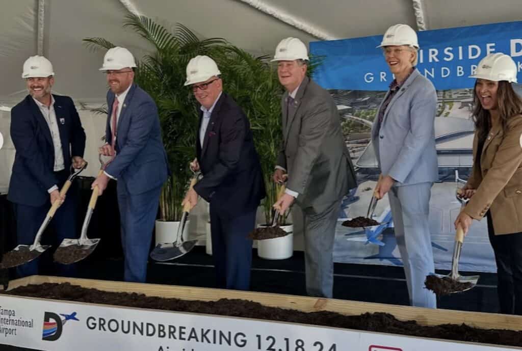 officials wear hard hats and toss dirt during a groundbreaking ceremony 