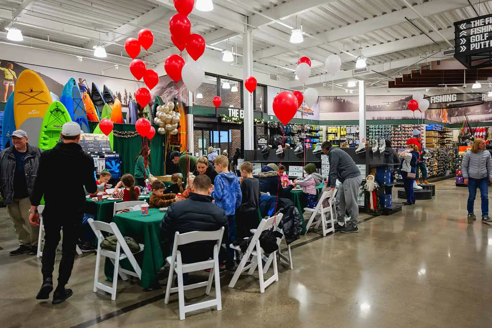 A holiday-themed event inside a store, featuring tables with activities for children, red and white balloons, and colorful kayaks displayed in the background.