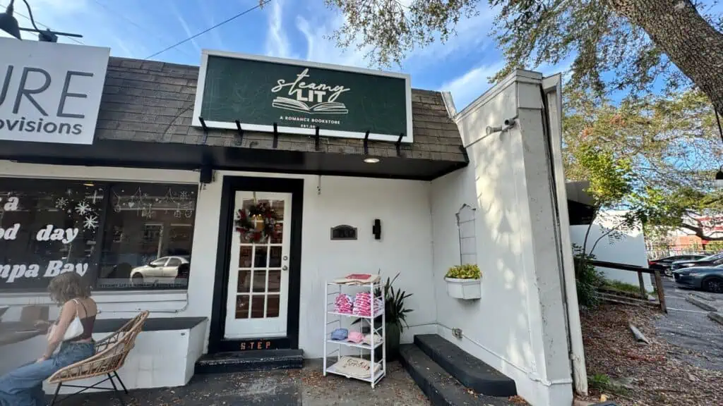 the exterior of steamy lit bookstore with a green store sign on a sunny blue sky day