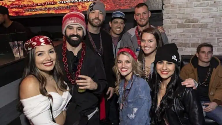 A group of friends dressed in pirate-themed outfits and accessories, smiling and posing at a lively bar.