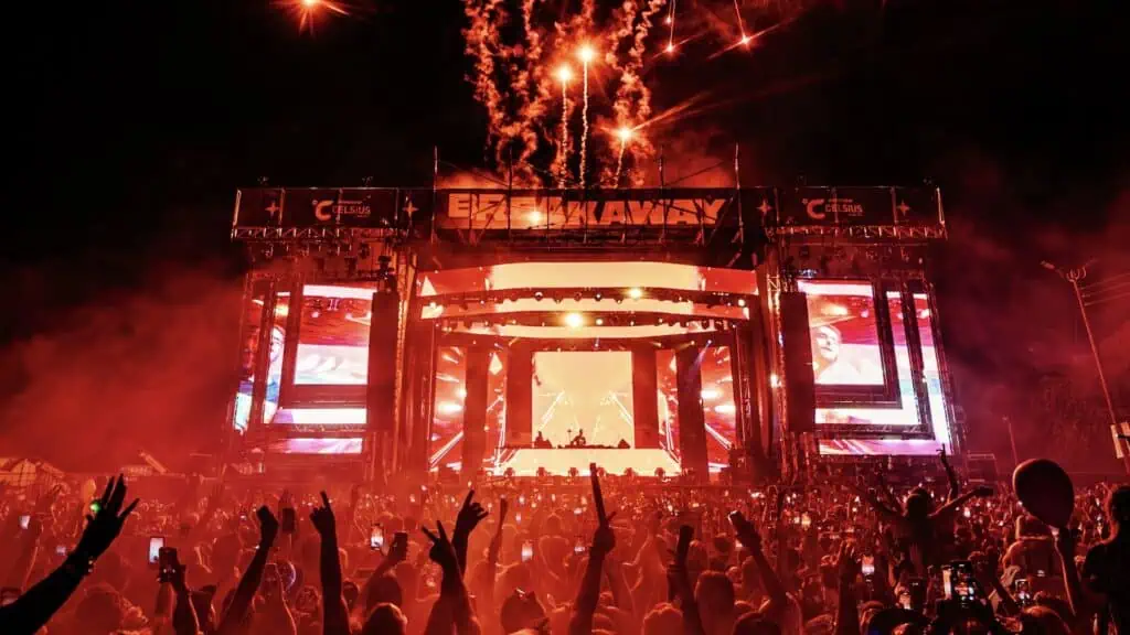 a large stage illuminated in red lights at night. Smoke machines add extra atmosphere on stage. the crowd's hands are in the air during the set.