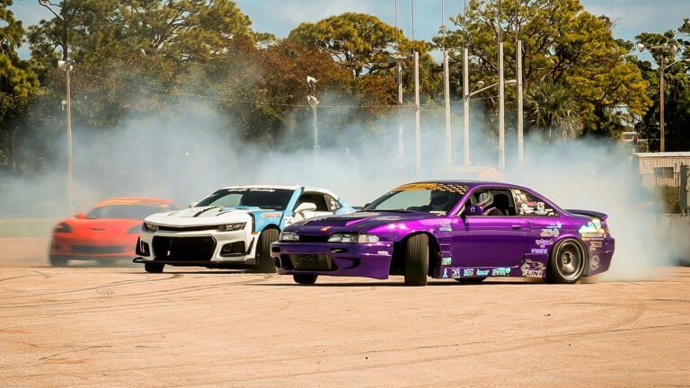 Multiple cars drifting in the dirt. The lead car is bright purple