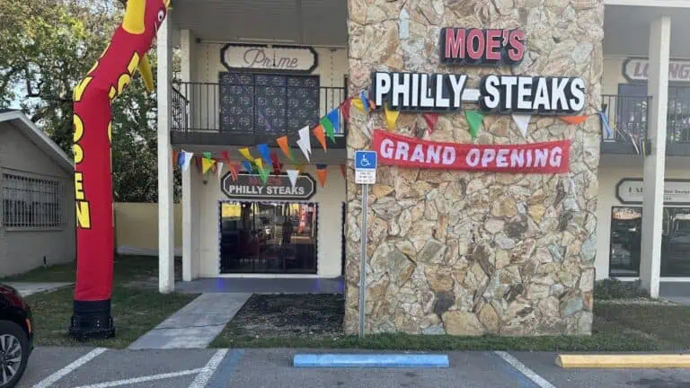 exterior of a cheesteak resraurant with a "Grand opening" banner on the stone facade of the restaurant