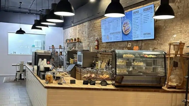 Interior of a cafe with multiple pastries on display and a menu illuminated above the espresso bar