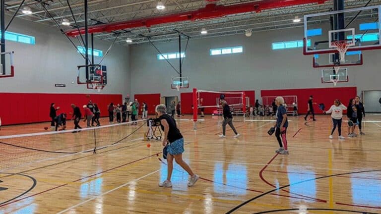 Interior of a large gym with multiple people playing pickleball/volleyball