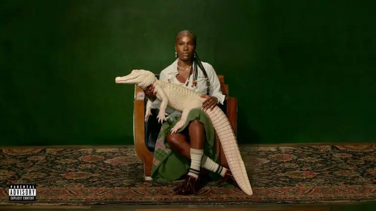 an artist holds an alligator on a sound stage. The backdrop is dark green.